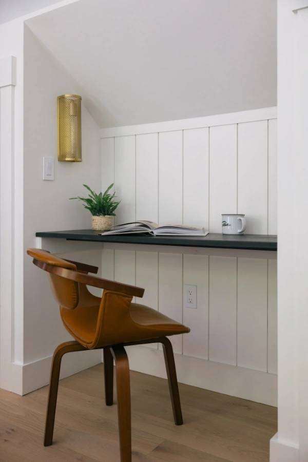 Minimal workspace nook with floating desk, leather chair, brass wall sconce, and paneled accent wall located in the master bedroom